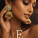 Fashion model gently touching her earrings, gold jhumka with blue stones and pearls shining under soft light, cinematic motion feel