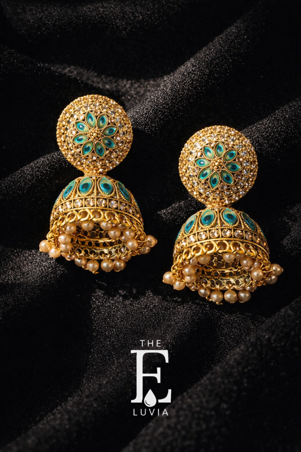 Gold traditional jhumka earrings with blue and green stones and pearl drops, placed on black textured fabric