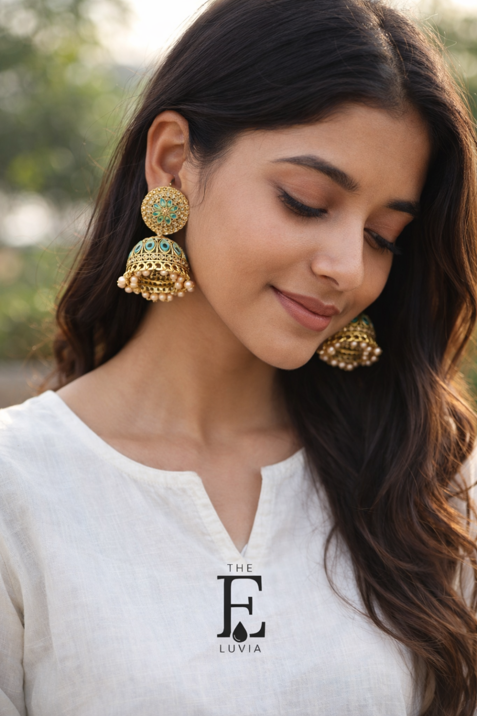 Young Indian woman wearing simple kurta, showcasing gold jhumka earrings with blue and pearl details, natural sunlight, outdoor background